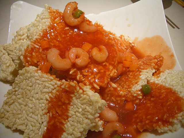Chunks of cooked rice covered with shrimp and red sweet and sour sauce. 