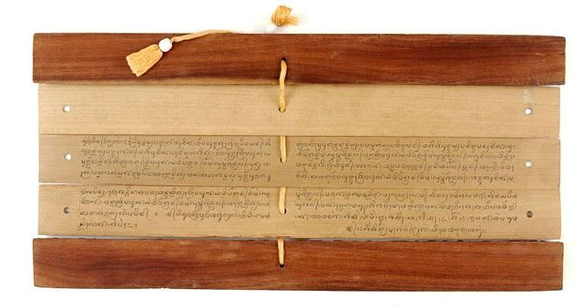 Rectangular strips of Lontar palm leaves with Balinese writing fastened together horizontally into a book with a cord woven through a hole in the middle of each leaf.